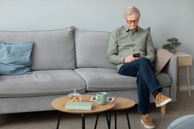 Hombre mayor que usa un teléfono inteligente sentado en un sofá en la sala de estar