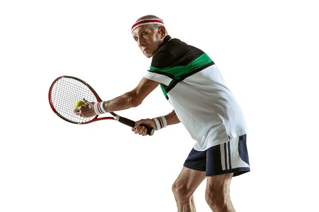 Hombre mayor con ropa deportiva jugando al tenis aislado en la pared blanca. Modelo masculino caucásico en gran forma se mantiene activo y deportivo. Concepto de deporte, actividad, movimiento, bienestar. Copyspace, anuncio.