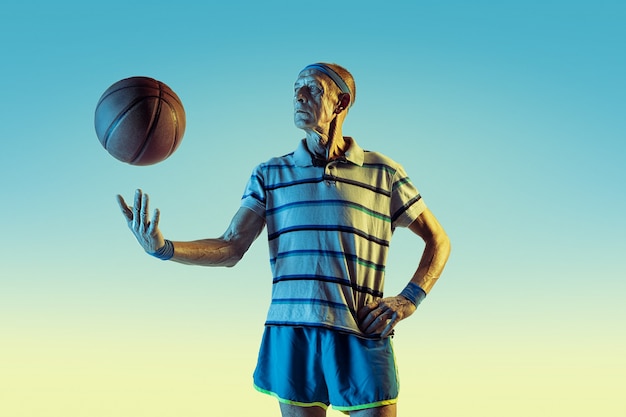Hombre mayor con ropa deportiva jugando baloncesto sobre fondo degradado, luz de neón.