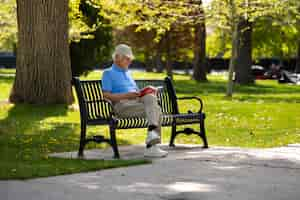 Foto gratuita hombre mayor sentado en un banco al aire libre y leyendo un libro