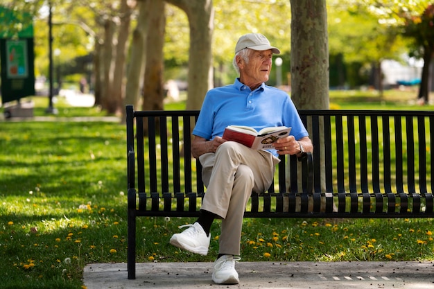 Hombre mayor sentado en un banco al aire libre y leyendo un libro