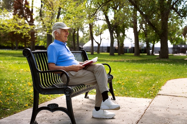 Hombre mayor sentado en un banco al aire libre y leyendo un libro