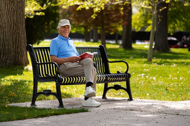 Hombre mayor sentado en un banco al aire libre y leyendo un libro