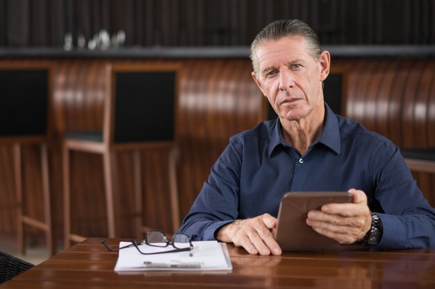 Hombre mayor serio con la tableta digital en el Café