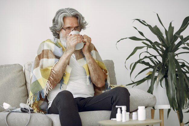 Hombre mayor solo sentado en el sofá. Hombre enfermo cubierto con cuadros escoceses. Grangfather con taza de té.