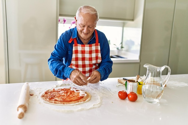 Hombre mayor sonriendo confiado cocinando pizza en la cocina