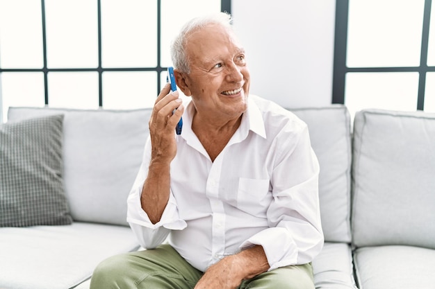 Hombre mayor sonriendo confiado usando un teléfono inteligente en casa