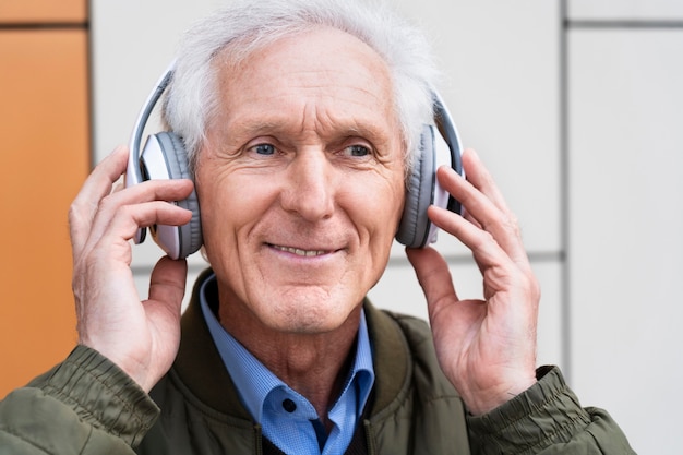 Hombre mayor sonriente en la ciudad escuchando música con auriculares