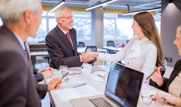 Foto gratuita hombre mayor sonriente que sacude las manos con la empresaria joven en la oficina