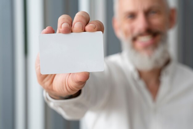 Hombre mayor sonriente que sostiene la tarjeta de visita en blanco