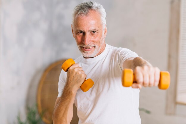 Hombre mayor sonriente sano que se resuelve con pesas de gimnasia