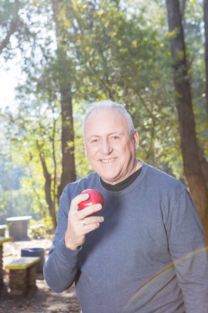 Hombre mayor sonriente sujetando una manzana después del ejercicio físico