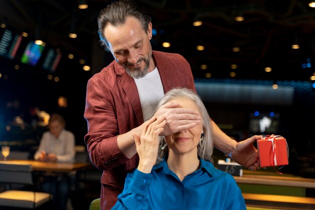 Hombre mayor sorprendiendo a su amigo con un regalo en un restaurante