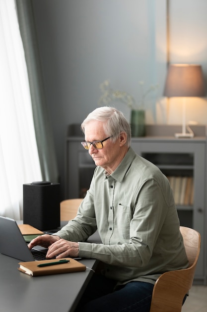 Foto gratuita el hombre mayor está usando una computadora portátil sentada en el escritorio en la sala de estar