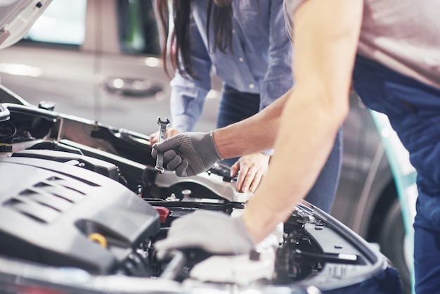 Un hombre mecánico y una mujer cliente miran el capó del automóvil y discuten las reparaciones