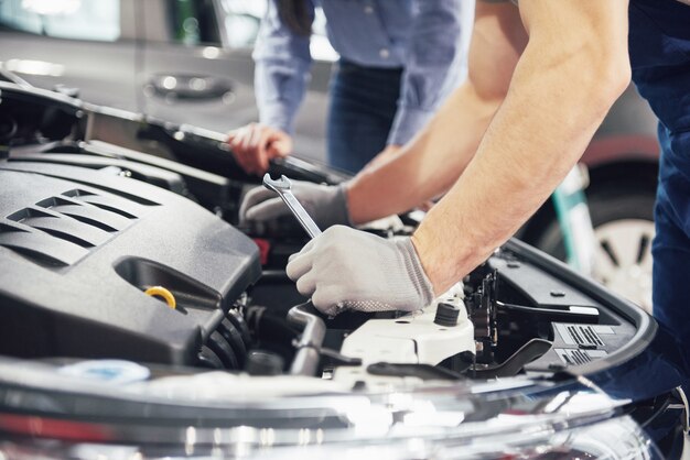 Un hombre mecánico y una mujer cliente miran el capó del automóvil y discuten las reparaciones