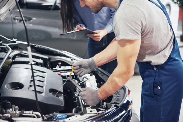 Un hombre mecánico y una mujer cliente miran el capó del automóvil y discuten las reparaciones