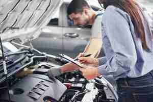 Foto gratuita un hombre mecánico y una mujer cliente miran el capó del automóvil y discuten las reparaciones