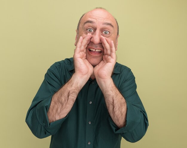 Hombre de mediana edad alegre con camiseta verde llamando a alguien aislado en la pared verde oliva