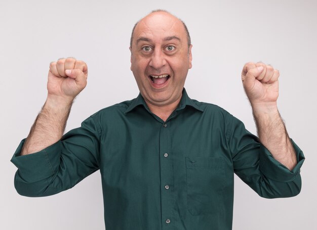 Hombre de mediana edad alegre con camiseta verde sosteniendo puños aislados en la pared blanca