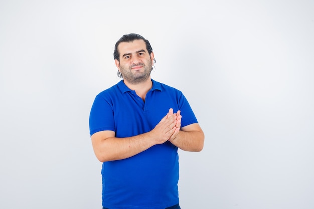 Hombre de mediana edad aplaudiendo en camiseta azul y mirando feliz