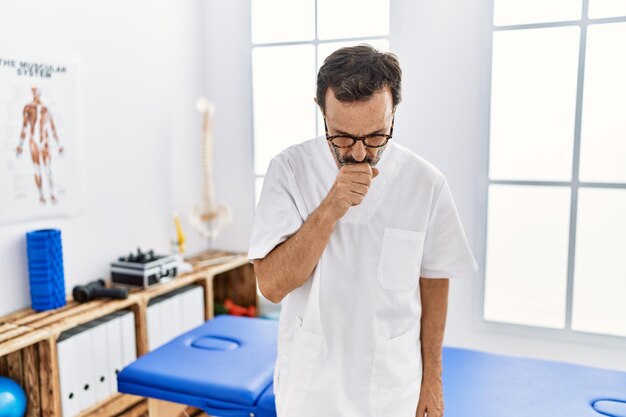 Hombre de mediana edad con barba que trabaja en la clínica de recuperación del dolor sintiéndose mal y tosiendo como síntoma del resfriado o bronquitis concepto de atención médica