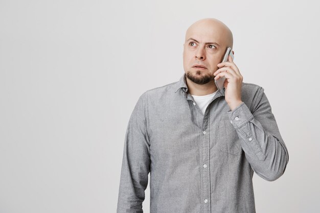 Hombre de mediana edad calvo pensativo pensando mientras habla por teléfono