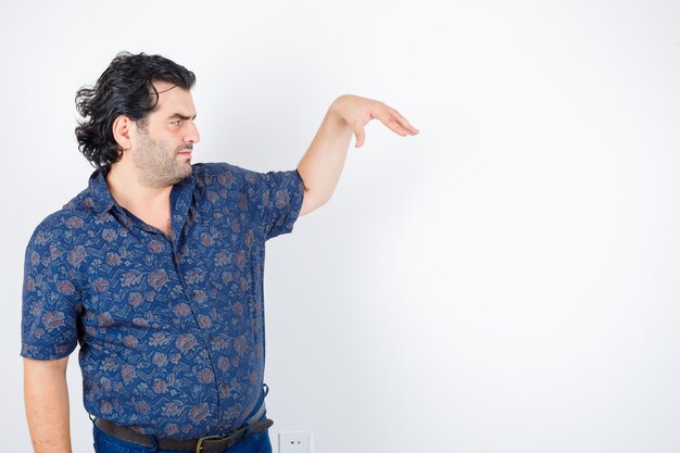 Hombre de mediana edad en camisa fingiendo sostener algo y mirando serio, vista frontal.