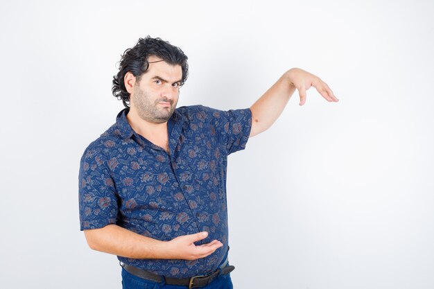 Hombre de mediana edad en camisa fingiendo sostener algo y mirando serio, vista frontal.