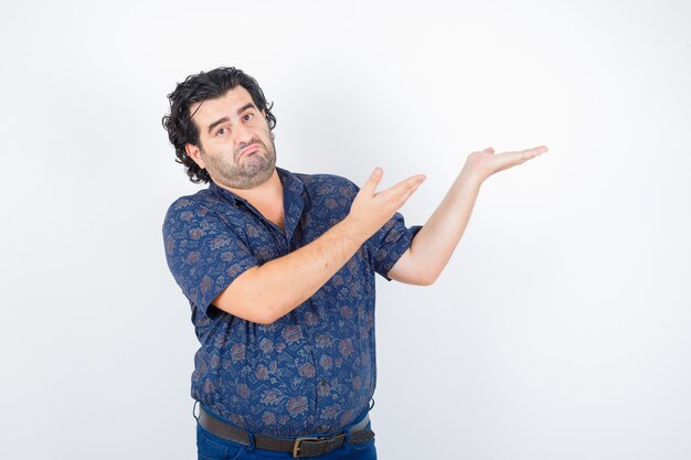 Hombre de mediana edad en camisa mostrando algo y mirando vacilante, vista frontal.