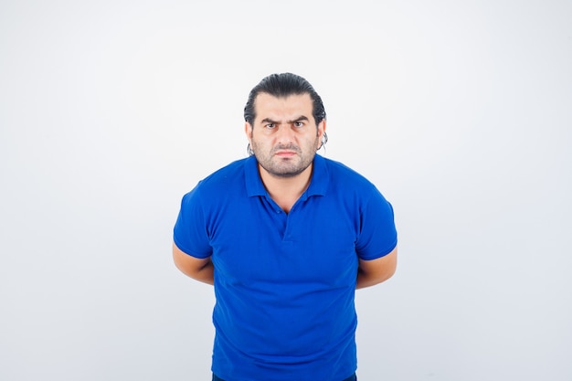 Hombre de mediana edad en camiseta azul mirando al frente mientras mantiene las manos detrás de la espalda