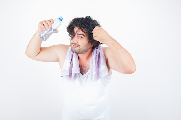 Hombre de mediana edad en camiseta sin mangas, toalla sosteniendo un mechón de cabello mientras mantiene la botella de agua y se ve divertido, vista frontal.