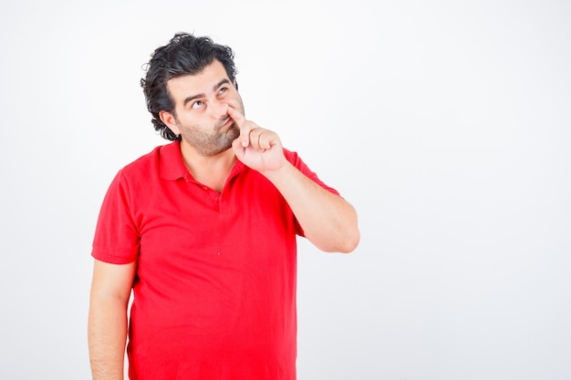 Foto gratuita hombre de mediana edad en camiseta roja asomando la nariz y mirando pensativo, vista frontal.