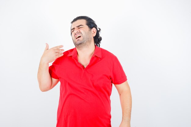 Hombre de mediana edad en camiseta roja levantando la mano sobre el hombro y mirando insatisfecho, vista frontal.