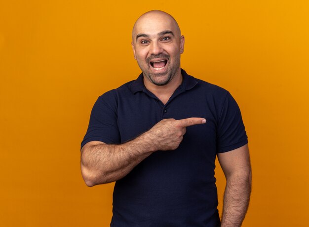 Hombre de mediana edad casual emocionado apuntando al lado aislado en la pared naranja