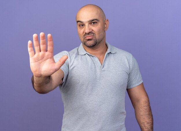 Hombre de mediana edad casual serio haciendo gesto de parada aislado en la pared púrpura