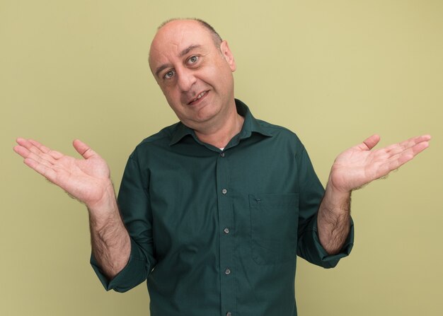 Hombre de mediana edad complacido con camiseta verde extendiendo las manos aisladas en la pared verde oliva