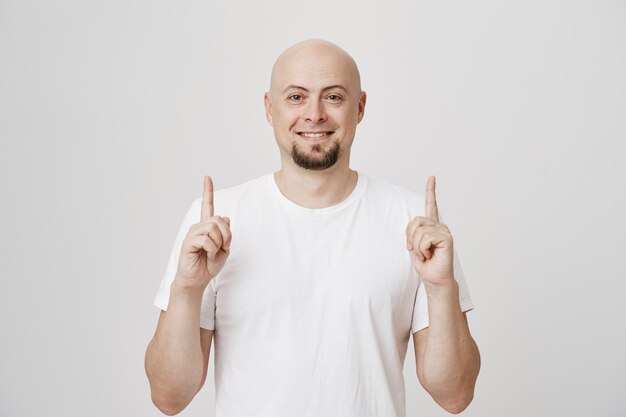 Hombre de mediana edad complacido sonriendo, señalando con el dedo hacia arriba