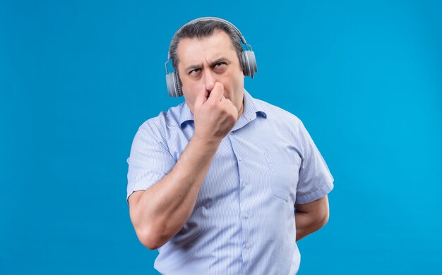 Hombre de mediana edad concentrado en camisa de rayas azules pensando en algo sosteniendo los dedos en la nariz en un espacio azul