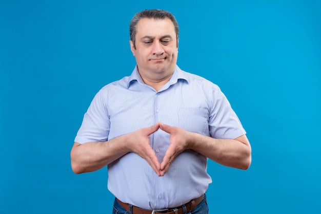 Hombre de mediana edad descontento y confundido en camisa de rayas azules pensando y tomados de la mano juntos en un espacio azul