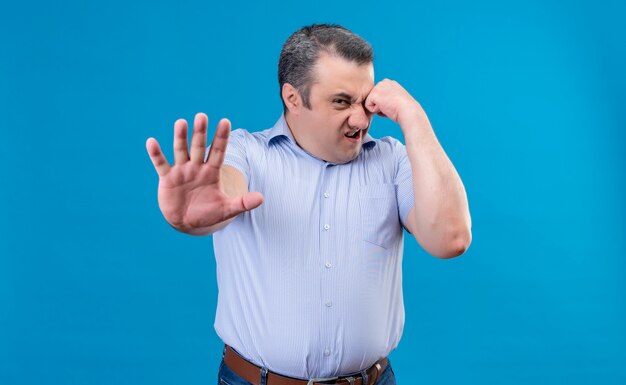 Hombre de mediana edad enojado y nervioso con camisa azul mostrando gesto de parada con las manos en un espacio azul