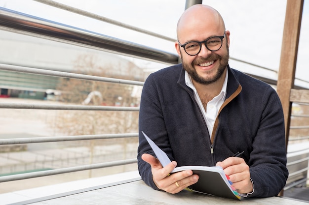 Hombre de mediana edad feliz que hace notas en café de la calle