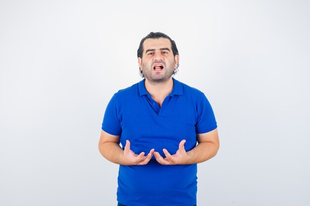 Hombre de mediana edad fingiendo sostener algo en una camiseta de polo y mirando pensativo. vista frontal.