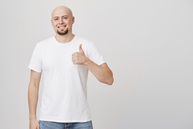 Hombre de mediana edad guapo satisfecho con la cabeza calva muestra el pulgar hacia arriba y sonriendo complacido