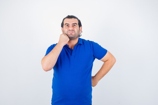 Hombre de mediana edad mirando hacia arriba en camiseta azul y mirando pensativo