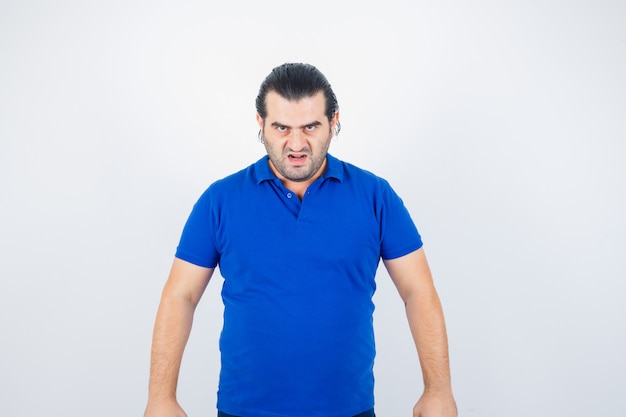 Hombre de mediana edad mirando a cámara en camiseta azul y mirando rencoroso