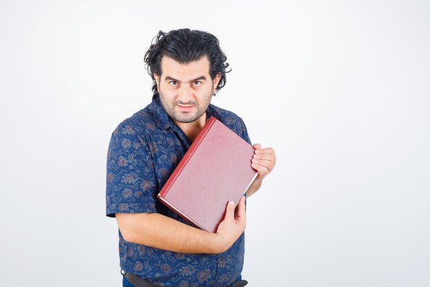 Hombre de mediana edad mirando a la cámara mientras sostiene el libro en camisa y parece seguro. vista frontal.