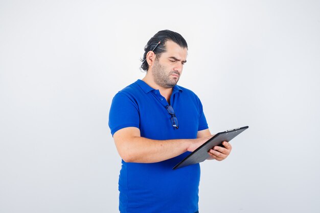 Hombre de mediana edad mirando documentos en el portapapeles en camiseta de polo y mirando enfocado. vista frontal.