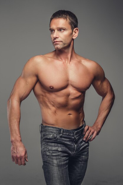 Hombre de mediana edad musculoso sin camisa en jeans posando en un estudio sobre un fondo gris.