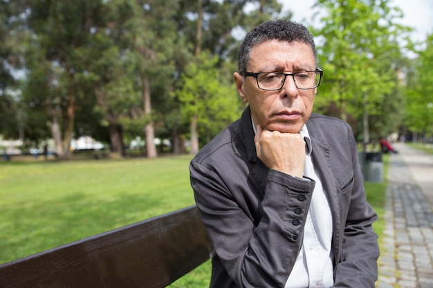 Hombre de mediana edad pensativo que se sienta en banco en parque de la ciudad